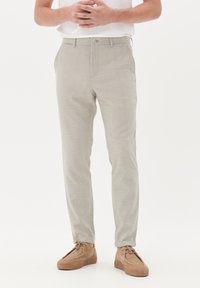 Light gray patterned trousers with a fitted design, featuring a button closure and pockets, paired with beige suede shoes.