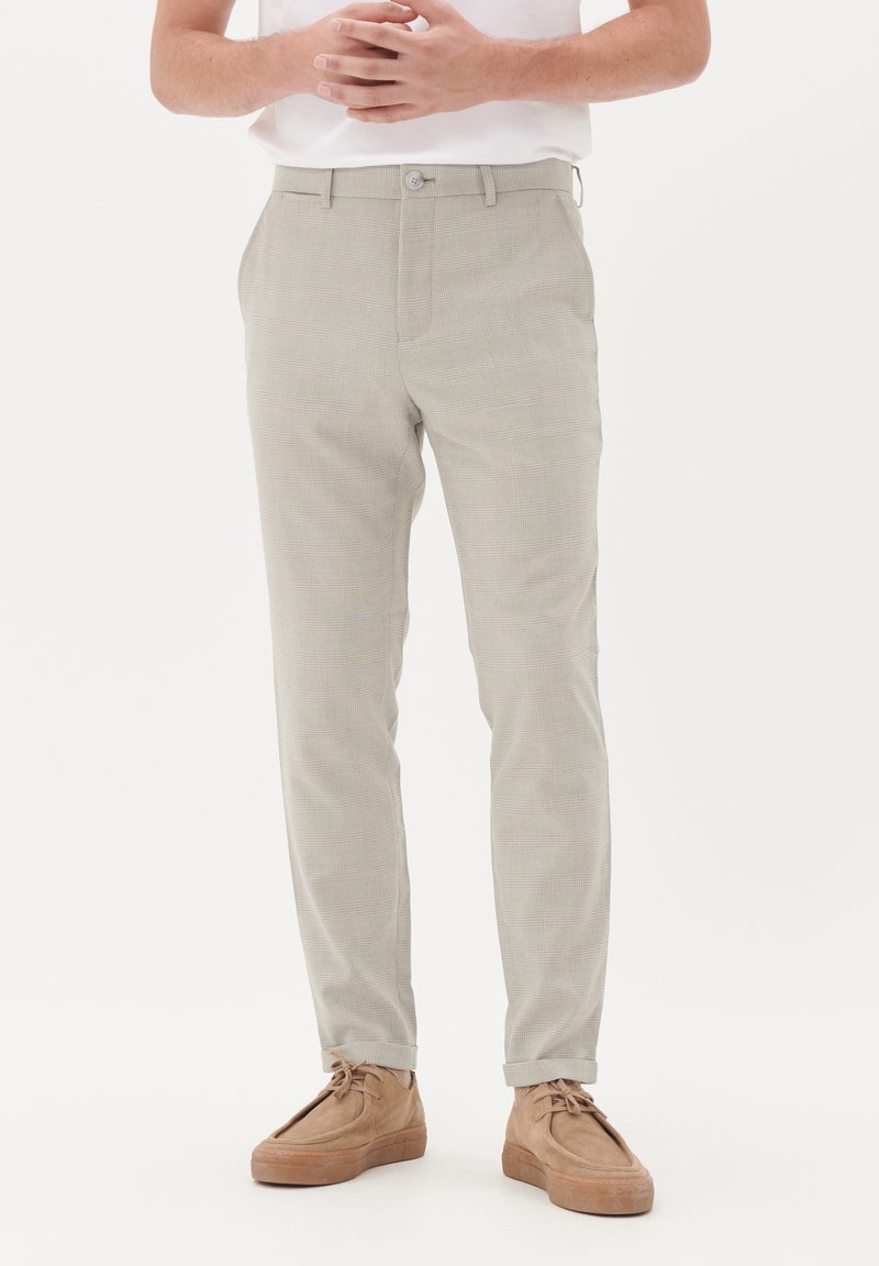 Light gray patterned trousers with a fitted design, featuring a button closure and pockets, paired with beige suede shoes.