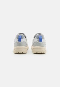 Baskets de sport grises et blanches avec une semelle texturée, une languette bleue à l'arrière, un matériau supérieur lisse et des accents en maille pour la respirabilité.