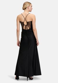 Czarna wieczorowa sukienka o dopasowanej górze, przezroczystym plecach i krzyżujących się ramiączkach, z długą, zwiewną spódnicą o delikatnym blasku.