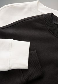 Nahaufnahme von gefalteten schwarz-weißen Sweatshirts mit gerippten Bündchen und Kragen auf neutralem Hintergrund.