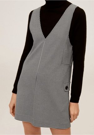 Schwarz-weißes Kleid mit Hahnentrittmuster, tiefem V-Ausschnitt, ärmellosem Design und Seitentasche. Der Stoff wirkt glatt und figurbetont.