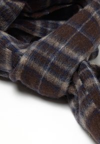 Sciarpa a scacchi marrone e blu realizzata in morbida lana, caratterizzata da una trama pelosa e un design allentato, con un nodo visibile nel tessuto.