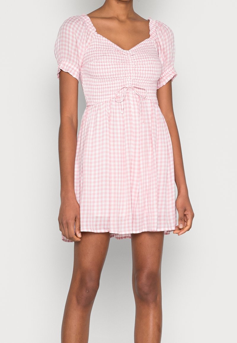Robe en vichy rose avec manches courtes bouffantes, corsage smocké et détail de lien à la taille. Tissu léger, jupe évasée.