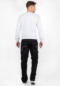 Felpa grigia con maniche lunghe, abbinata a pantaloni cargo neri con cuciture bianche e numerosi taschini, vista da dietro.