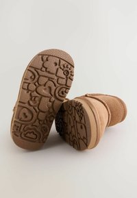 Cizme din suede maro până la gleznă cu tălpi din cauciuc texturat, având modele jucăușe, inclusiv inimi și nori, și un design robust.