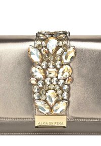 Clutch metálica dorada con un adorno joyado que presenta piedras transparentes y de color ámbar. Textura suave, forma rectangular y placa con el logotipo.