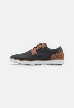 Chaussures pour hommes présentant un dessus en tissu gris foncé, des accents en cuir marron, une semelle en caoutchouc blanche, et un design minimaliste avec un laçage.