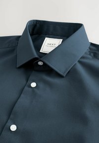 Tummansininen napituspaita, joka on valmistettu sileästä kankaasta. Paidassa on terävä kaulus, valkoiset napit ja siinä on etiketti, jossa lukee "NEXT TAILORING."