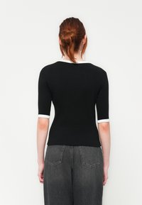 Tett svart topp med korte ermer som har hvit kanting rundt halsen og ermene. Jevn tekstur, minimal design og ingen synlige mønstre.
