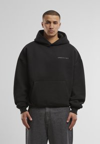 Schwarzer Hoodie aus Baumwollmischgewebe, mit einer Vorderwärtasche und dem Text "VERBOTEN" in hellerem Farbton. Übergrößenpassform mit gerippten Bündchen.