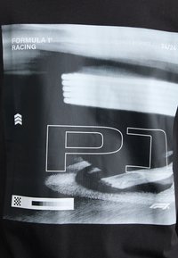 Sort T-shirt med et stort monochromt grafik, der har teksten "FORMULA 1® RACING", mønstre der ligner racerbane, og et F1-logo.
