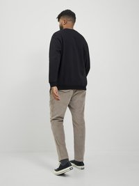 Black sweatshirt, beige corduroy pants, and black sneakers. The outfit features a textured finish and a relaxed fit.