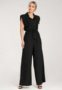Czarny kombinezon z kołnierzem, z guzikami, szerokimi nogawkami, paskiem w talii i akcentami na ramionach. Gładka faktura materiału i dopasowany krój.