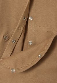 Close-up of beige fabric with silver snap buttons, showing open and closed fasteners and detailed stitching on a garment.