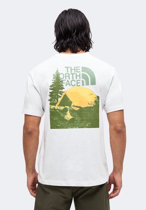 Vue de dos d'une personne portant un t-shirt blanc avec une scène de camping en vert et jaune, tente, arbre et logo "The North Face" dans le dos.