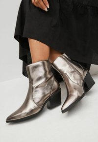 Botines de tobillo plateados metálicos con punta afilada, diseño elegante, acabado texturizado y tacón grueso. Cierre de cremallera en el lateral para una fácil puesta.
