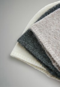 Trzy nałożone na siebie próbki tkaniny w kolorach szarym, jasnobeżowym i białym. Każda ma miękką, teksturowaną powierzchnię z widocznymi włóknami i wzorem dzianym.