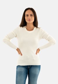 Maglione bianco a costine con maniche lunghe, dotato di bottoni sulle spalle e un colletto rotondo, abbinato a jeans blu.