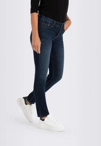 Tummansiniset slim fit -farkut puhtaalla suunnittelulla, vaalealla ompelulla ja vetoketjulla. Yhdistettynä valkoisiin tennareihin, joissa on musta kantapäähahmo.