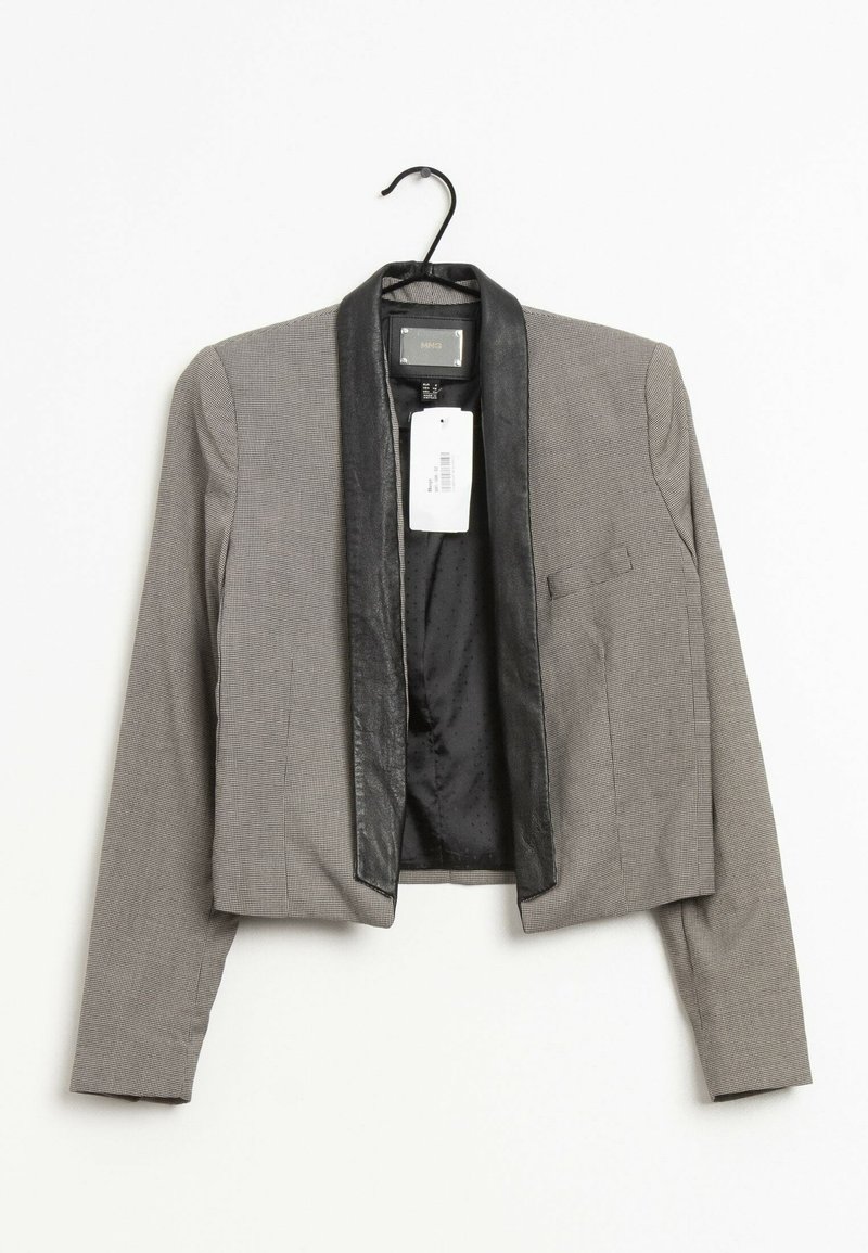 Blazer gris court avec des revers en satin noir accroché à un cintre noir sur fond blanc.