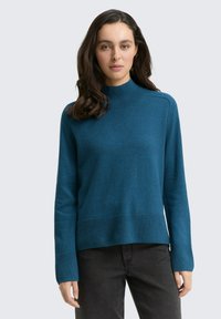 Türkisfarbener gestrickter Pullover mit einem hohen Kragen, langen Ärmeln und gerippten Bündchen und Saum. Glatte Textur, entspannte Passform und minimale Details.