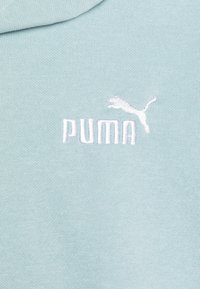 Felpa con cappuccio di colore azzurro chiaro con una texture morbida. Presenta un logo "PUMA" ricamato in bianco e un design minimalista di un gatto in movimento.