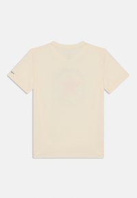 Camiseta de color crema de manga corta con cuello redondo y textura suave, que presenta un diseño gráfico de estrella en color rosa claro en la parte trasera.