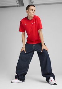 Rød kortærmet T-shirt med logo, oversized blå denimbukser og hvide sportsko med røde detaljer. Glat stof og løs pasform.