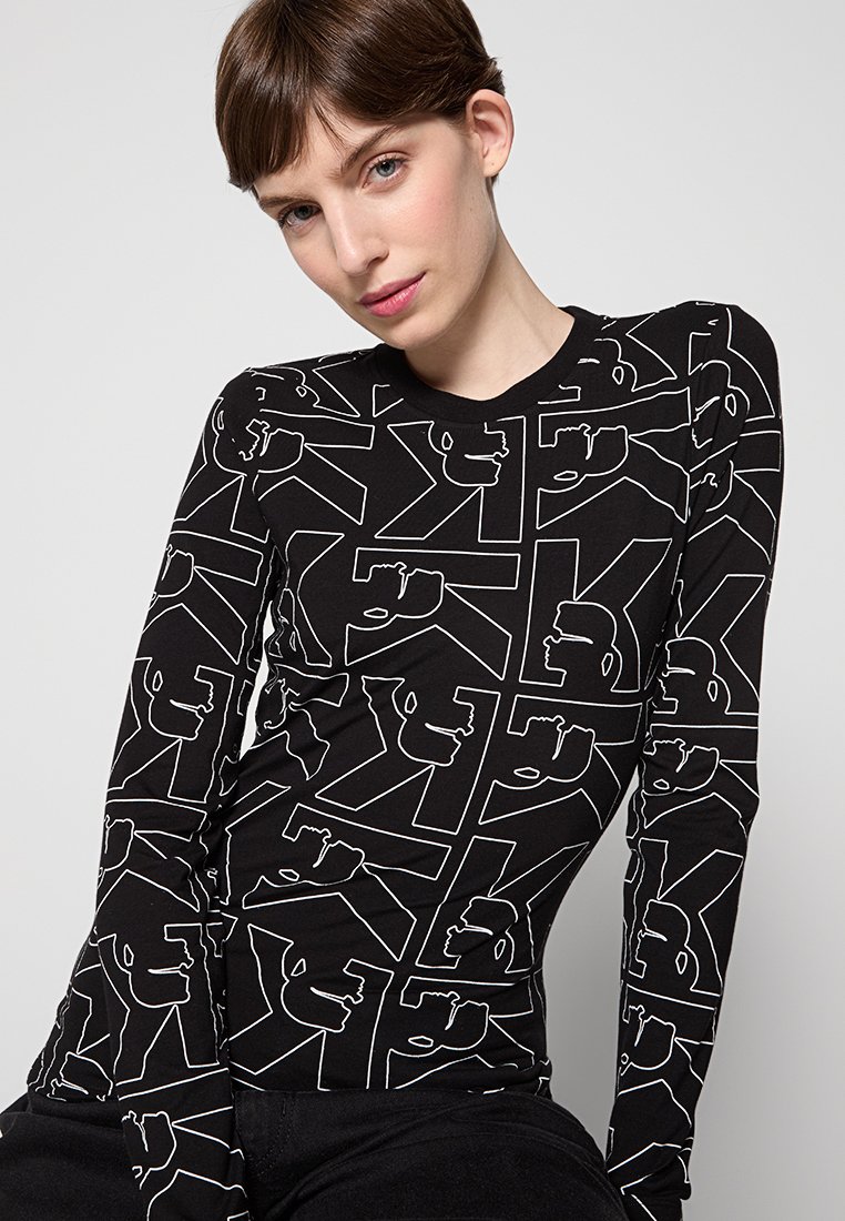 Maglia nera a maniche lunghe con un motivo geometrico di contorni bianchi di volti. Tessuto morbido con scollatura a girocollo e design aderente.