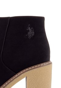 Bottine en daim noir avec un talon épais marron clair et un logo discret embossé représentant un joueur de polo à cheval.