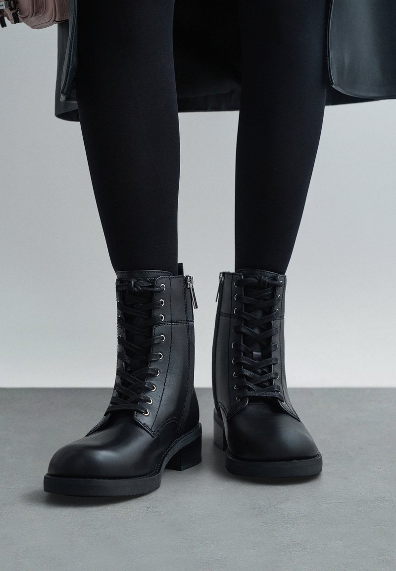 Mustad mustad nahast pahkluu saapad, millel on paelad ees ja külgmised tõmblukud. Paksemad tallad ja ruudukujuline varvas. Sile tekstuur koos peente õmblusdetailidega.