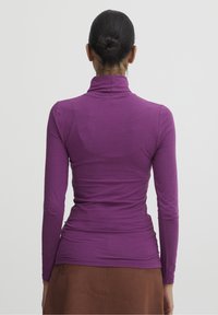 Långärmad topp i lila stretchmaterial med design av hög krage, åtsittande silhuett och mjuk textur, tillsammans med en brun kjol.