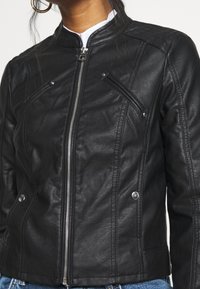 Svart faux lädermotorcykeljacka med ståkrage, dragkedja fram, texturerade detaljer och diagonala bröstfickor.