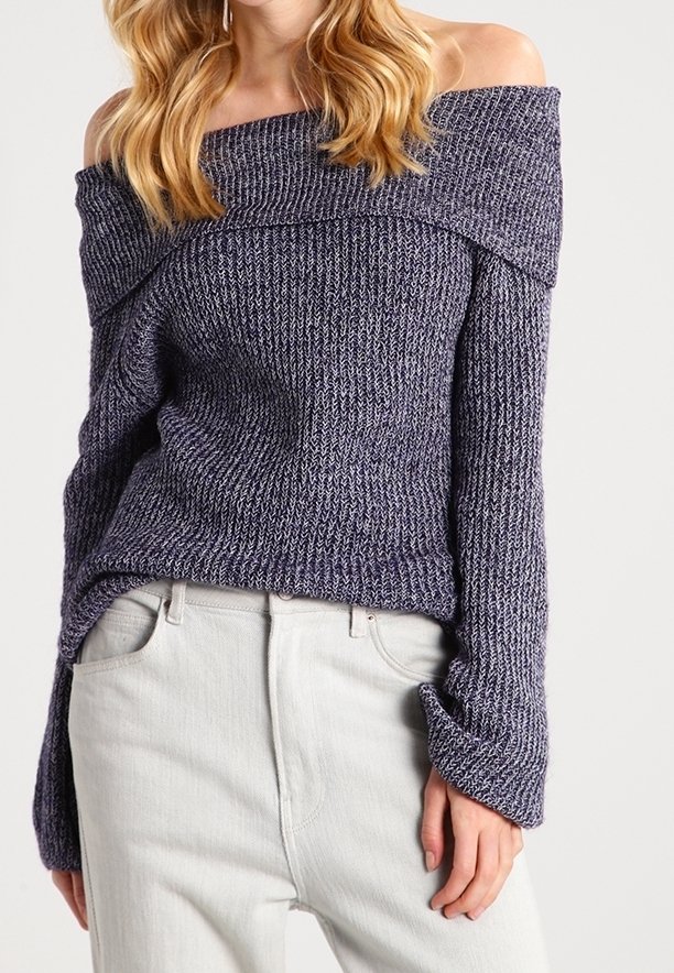 Femme portant un pull en maille violet à épaules dénudées avec des manches longues et un pantalon taille haute de couleur claire.