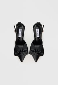 Schwarze Slingback-Pumps mit hohen Absätzen, spitzen Zehen und einer markanten Schleifendetail vorne, mit Lederstruktur und Knöchelriemen.