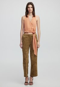 Top a halter pesca con dettaglio a cravatta, abbinato a pantaloni a gamba larga texturizzati color khaki. La modella indossa sandali marroni, presentando un look casual.