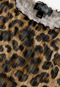 Leopardenmuster-Stoff in Schwarz- und Brauntönen. Wellenförmiger Ausschnitt und weiches, strukturiertes Material. Das Etikett trägt die Aufschrift "Maternity Next".