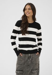 Pull à rayures noires et blanches avec manches longues, encolure ronde et poignets côtelés. Matière en maille douce avec des rayures horizontales contrastées.