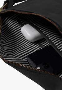 Schwarze Tasche mit geöffnetem Reißverschluss, der gestreiften Innenausstattung zeigt, eine weiße Hülle für kabellose Ohrhörer und ein teilweise sichtbares schwarzes Smartphone darin.