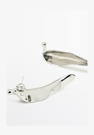 Par af skinnende, uregelmæssigt formede sølvøreringe med stiftbagstykke på hvid baggrund.