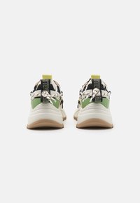 Une paire de baskets épaisses avec des semelles blanches, des accents verts et noirs, des languettes de talon noires étiquetées "STEVE MADDEN" et des lacets beige et blancs noués à l'arrière.