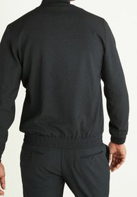 Czarna teksturowana kurtka z kołnierzem na zamek, ściągaczami na mankietach i pasie; posiada subtelny wzór w kratkę, w parze z dopasowanymi czarnymi spodniami.