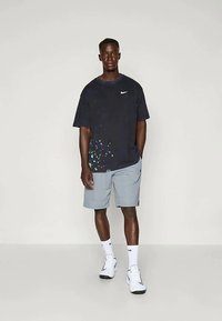 Marinesblå Nike T-shirt med korte ærmer og farverigt splatter-design; kombineret med lysegrå træningsshorts, hvide sokker og sneakers.