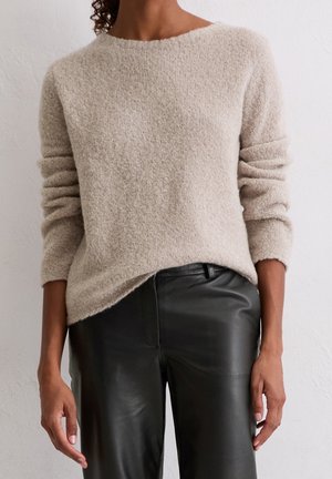 Beige textured long-sleeve sweater paired with black leather pants, worn by person standing against a plain light wall.