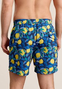Shorts de bain pour hommes en tissu bleu foncé présentant un motif de citrons et de feuilles en jaune et vert. Taille élastique avec une poche arrière.