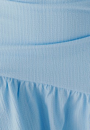 Světlomodrá texturovaná tkanina má hladkou horní část a na spodku shrnutý volánek, který vytváří plynulý design.