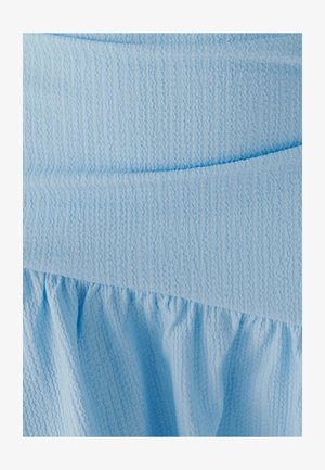 Světlomodrá texturovaná tkanina má hladkou horní část a na spodku shrnutý volánek, který vytváří plynulý design.