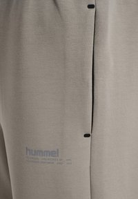 Lysegrå træningsbukser med en blød tekstur, med sorte accenter, sidelommer og et logo trykt i blåt nær kanten.