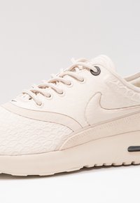 Baskets Nike beige clair avec tissu texturé, fermeture à lacets et amorti à air visible dans la semelle, présentées en angle pour montrer le côté extérieur.